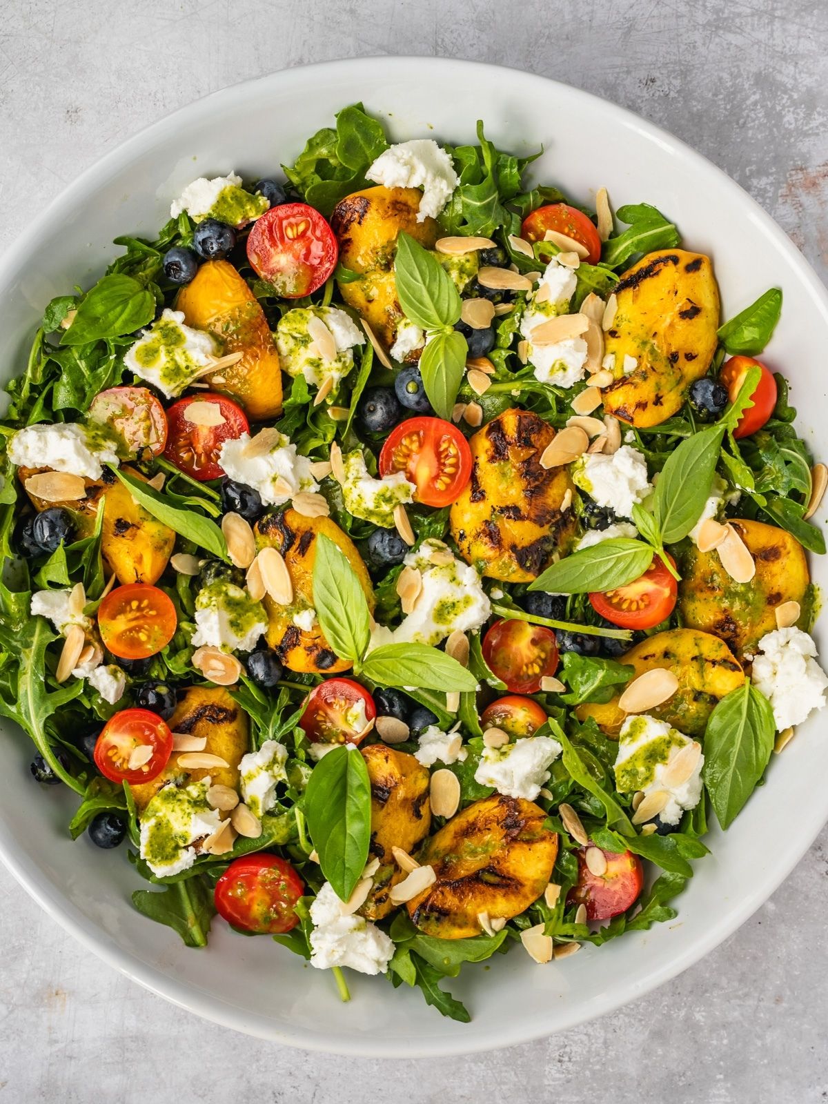 Grilled peach salad with basil, arugula, blueberries and goat cheese in a large serving tray.