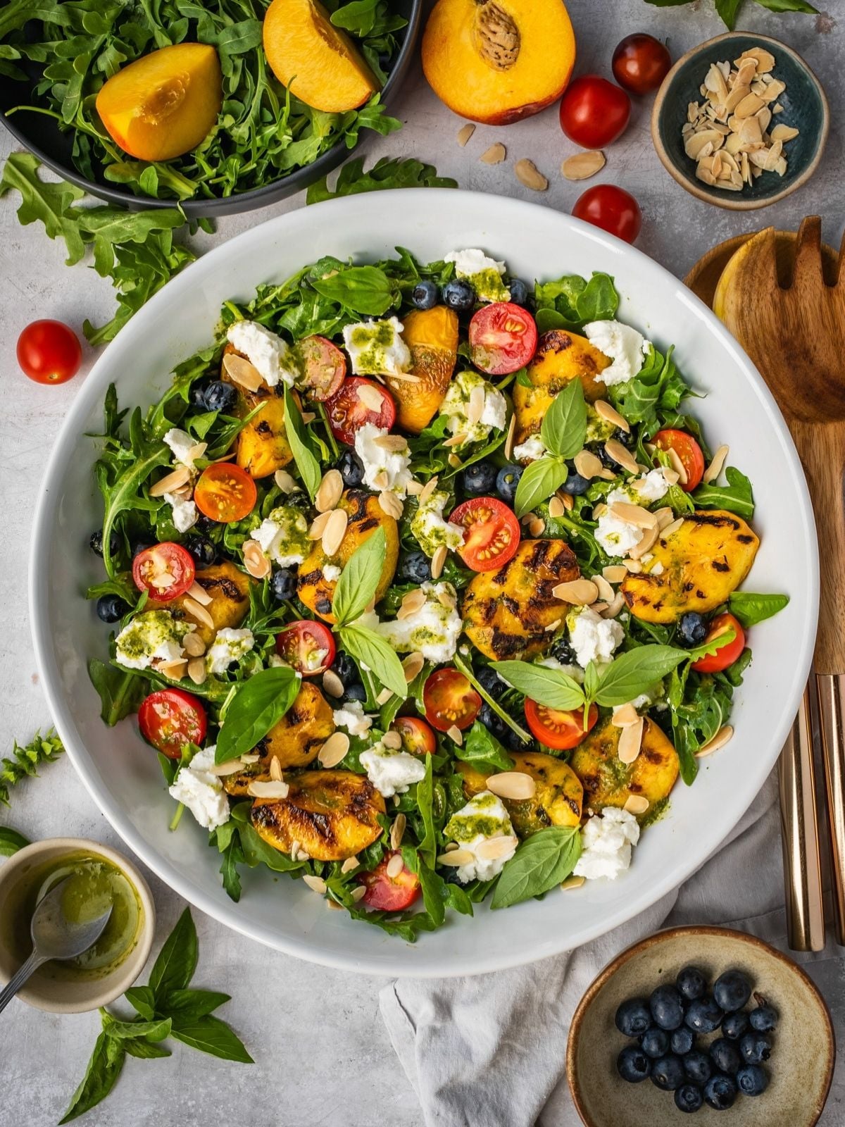 Grilled peach salad with basil, arugula, blueberries and goat cheese in a large serving tray.