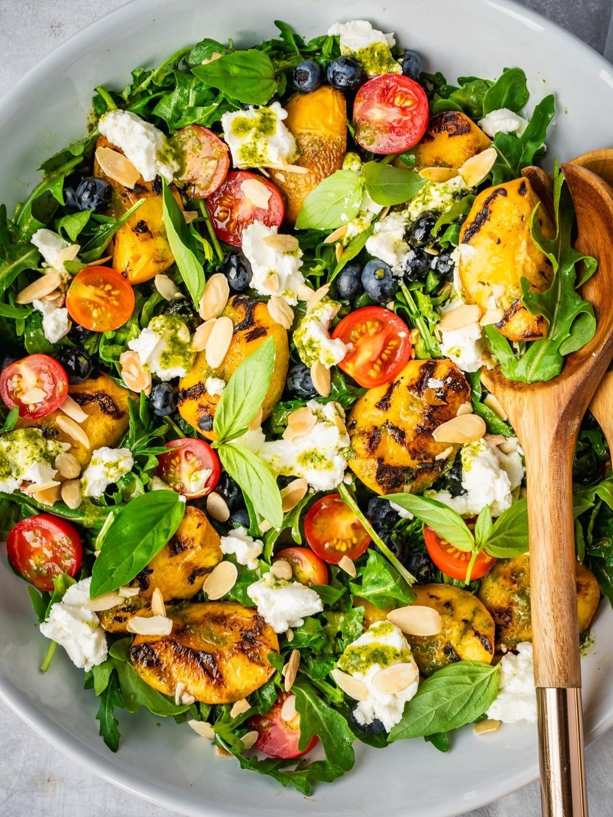 Grilled peach salad with basil, arugula, blueberries and goat cheese in a large serving tray.
