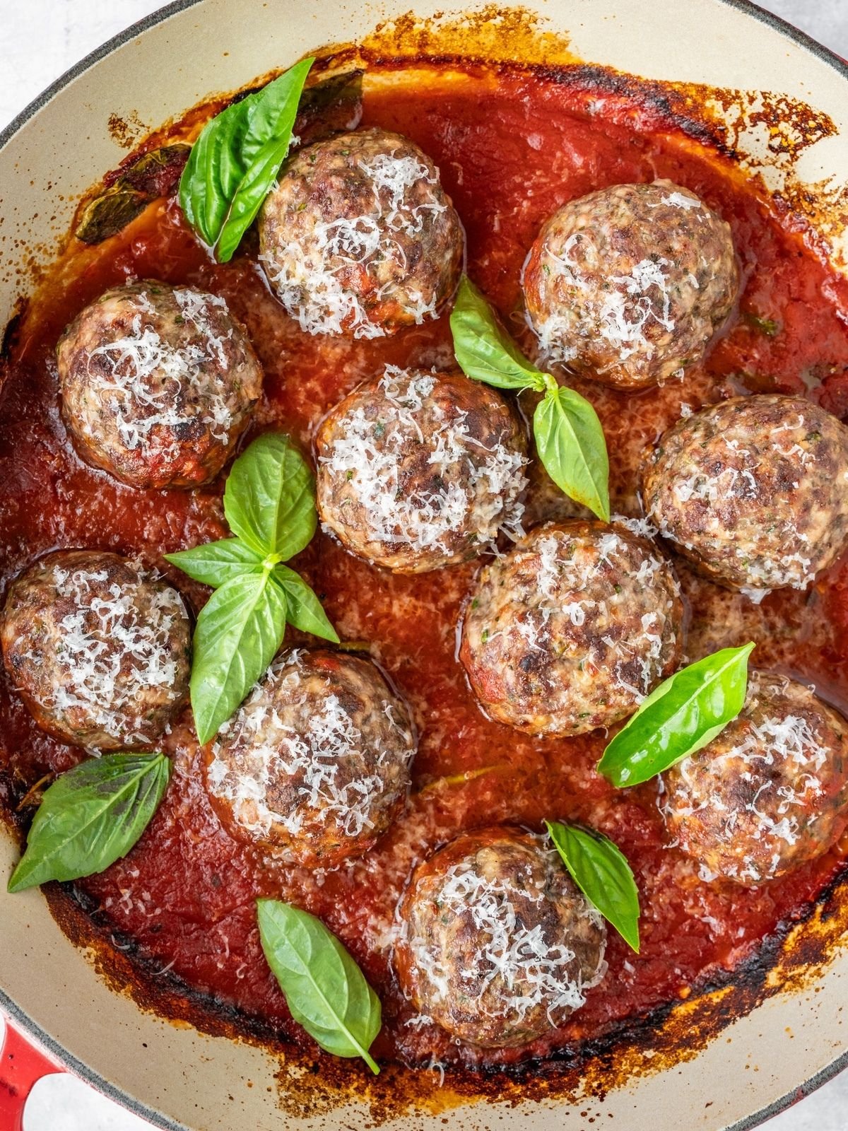 Italian Meatballs simmering in marinara, garnished with fresh basil and Parmesan.