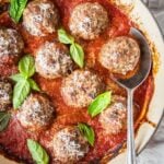 Italian Meatballs simmering in marinara, garnished with fresh basil and Parmesan.