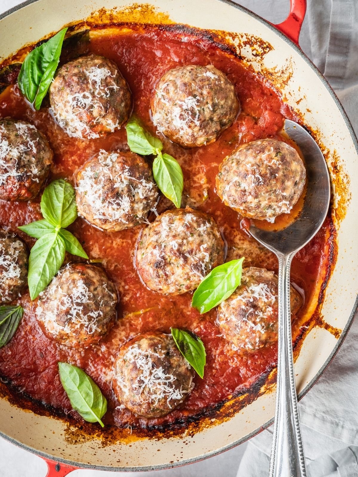 Italian Meatballs simmering in marinara, garnished with fresh basil and Parmesan.