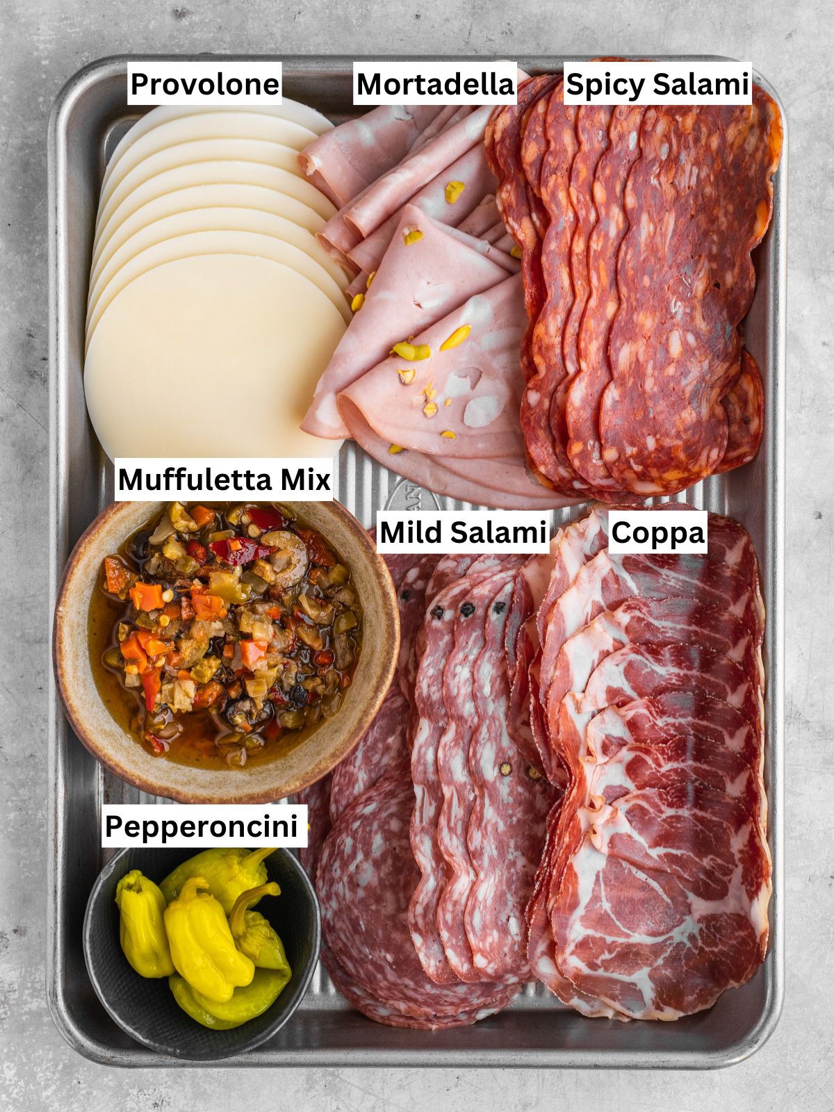 Muffuletta sandwich recipe ingredients with individual labels on a metal tray.