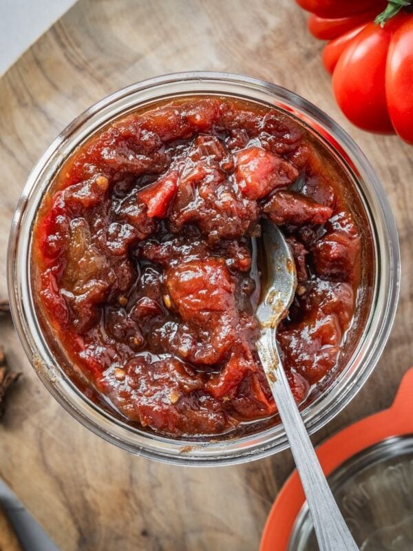 A mason jar filled to the top with savory and sweet tomato jam, sitting on a wooden board.