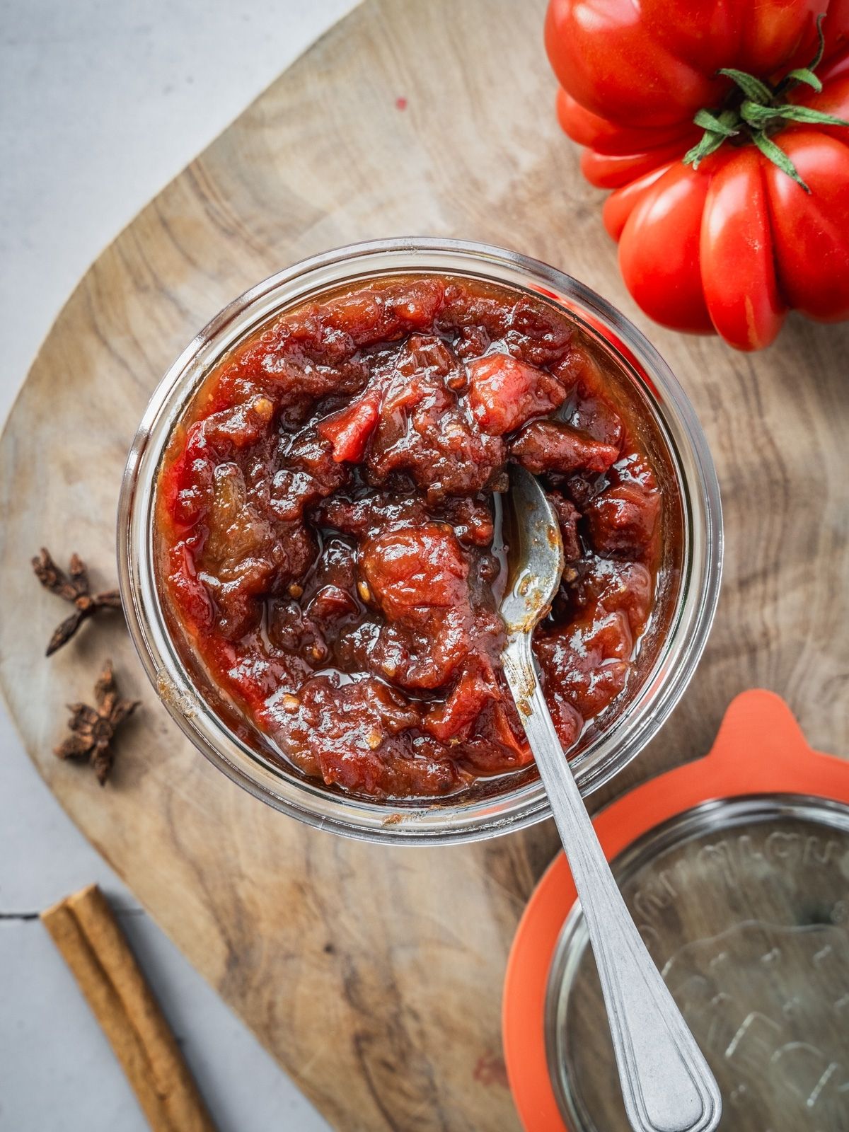 A mason jar filled to the top with tomato jam, sitting on a wooden board.