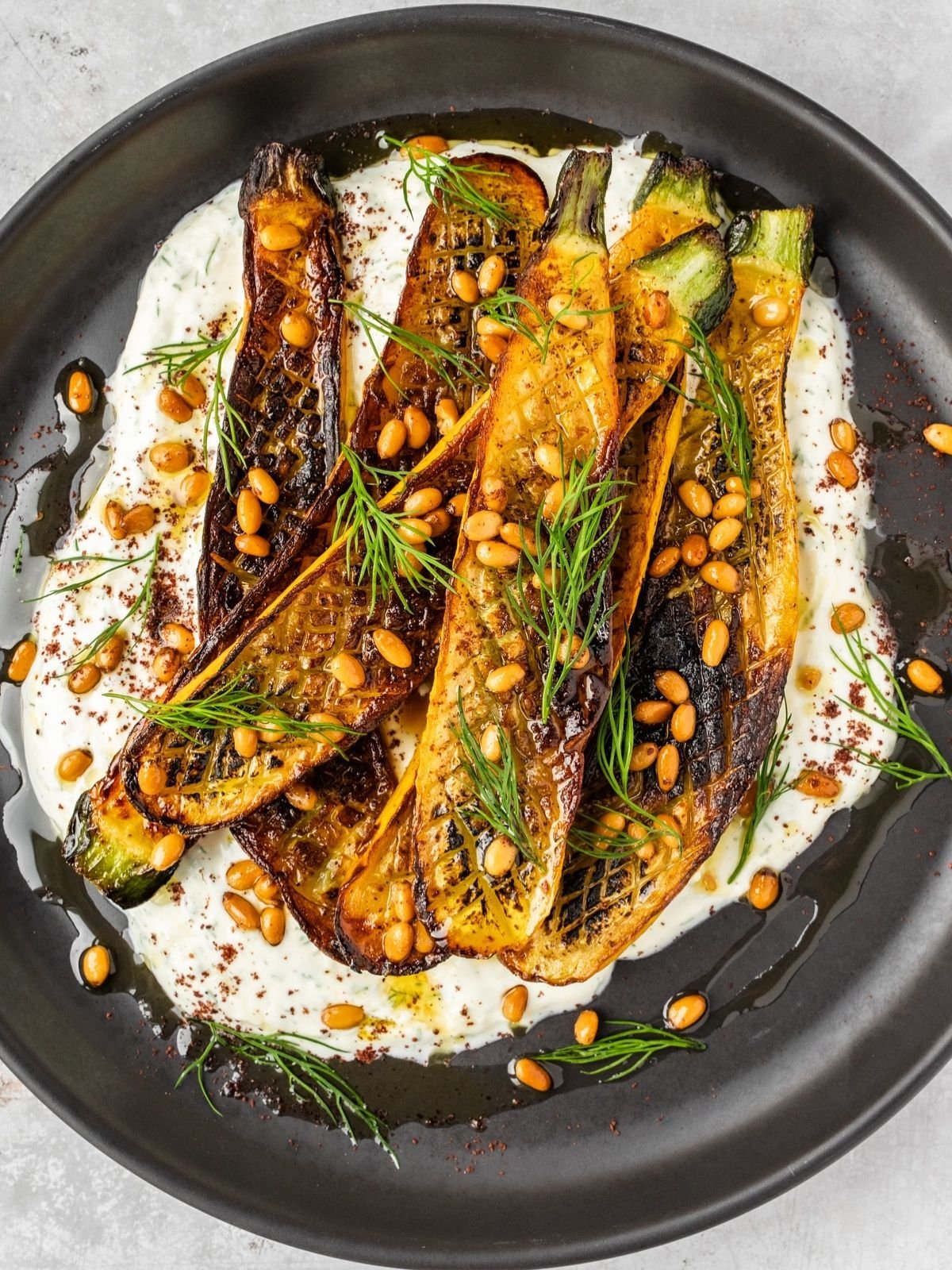 Charred zucchini over garlic yogurt garnished with pine nuts and dill.