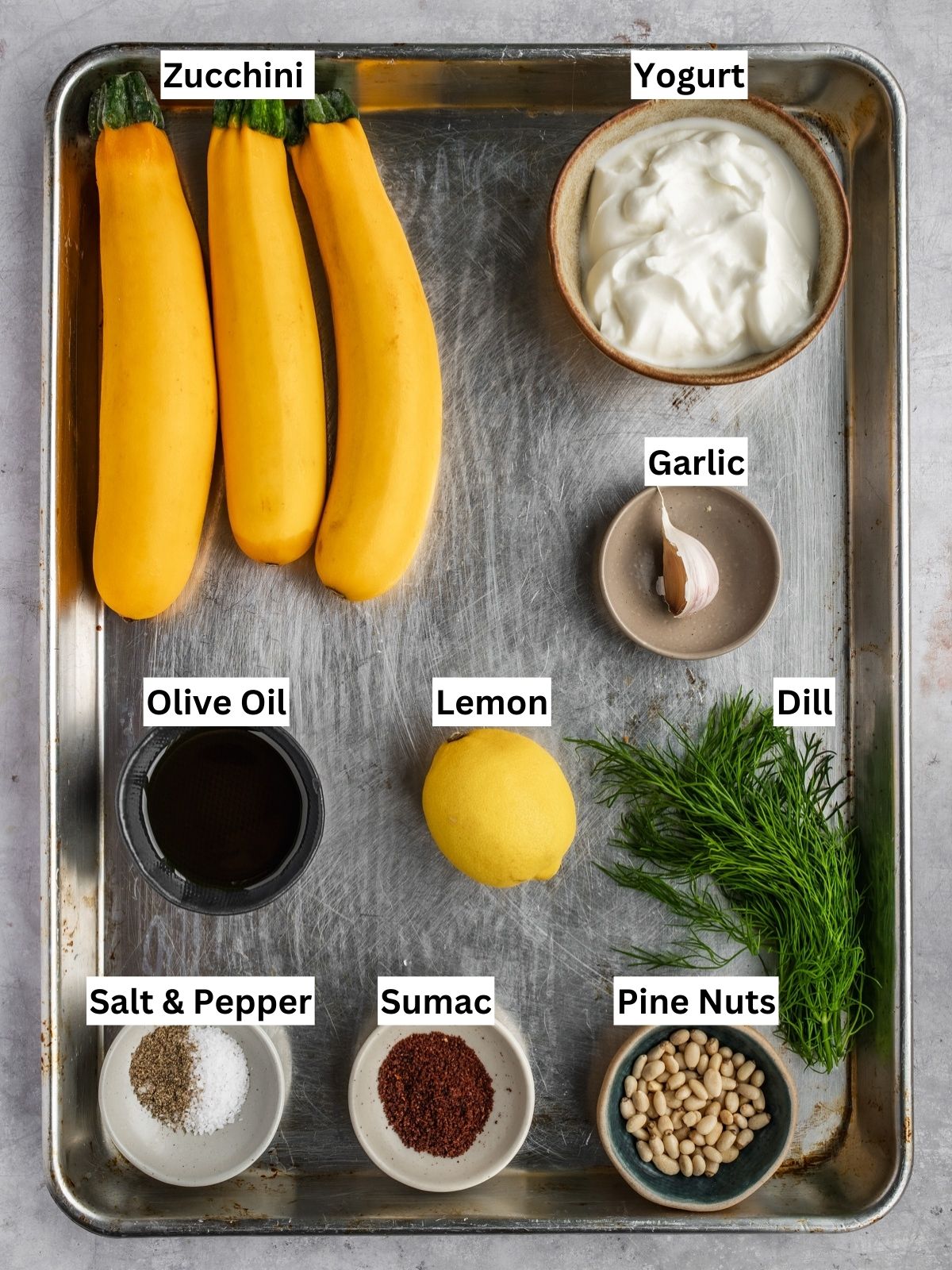 Charred zucchini over garlic yogurt recipe ingredients with individual labels on a metal tray.