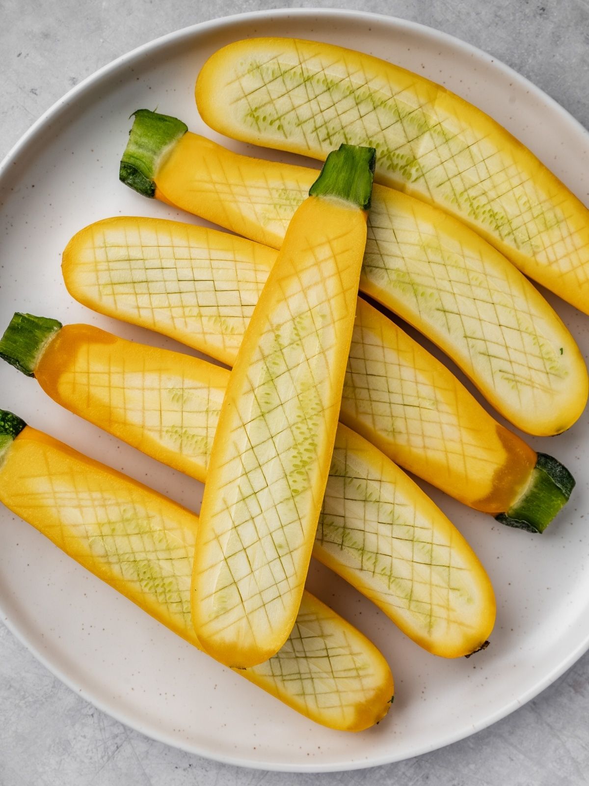 Zucchini halves scored with a paring knife in a diamond pattern.