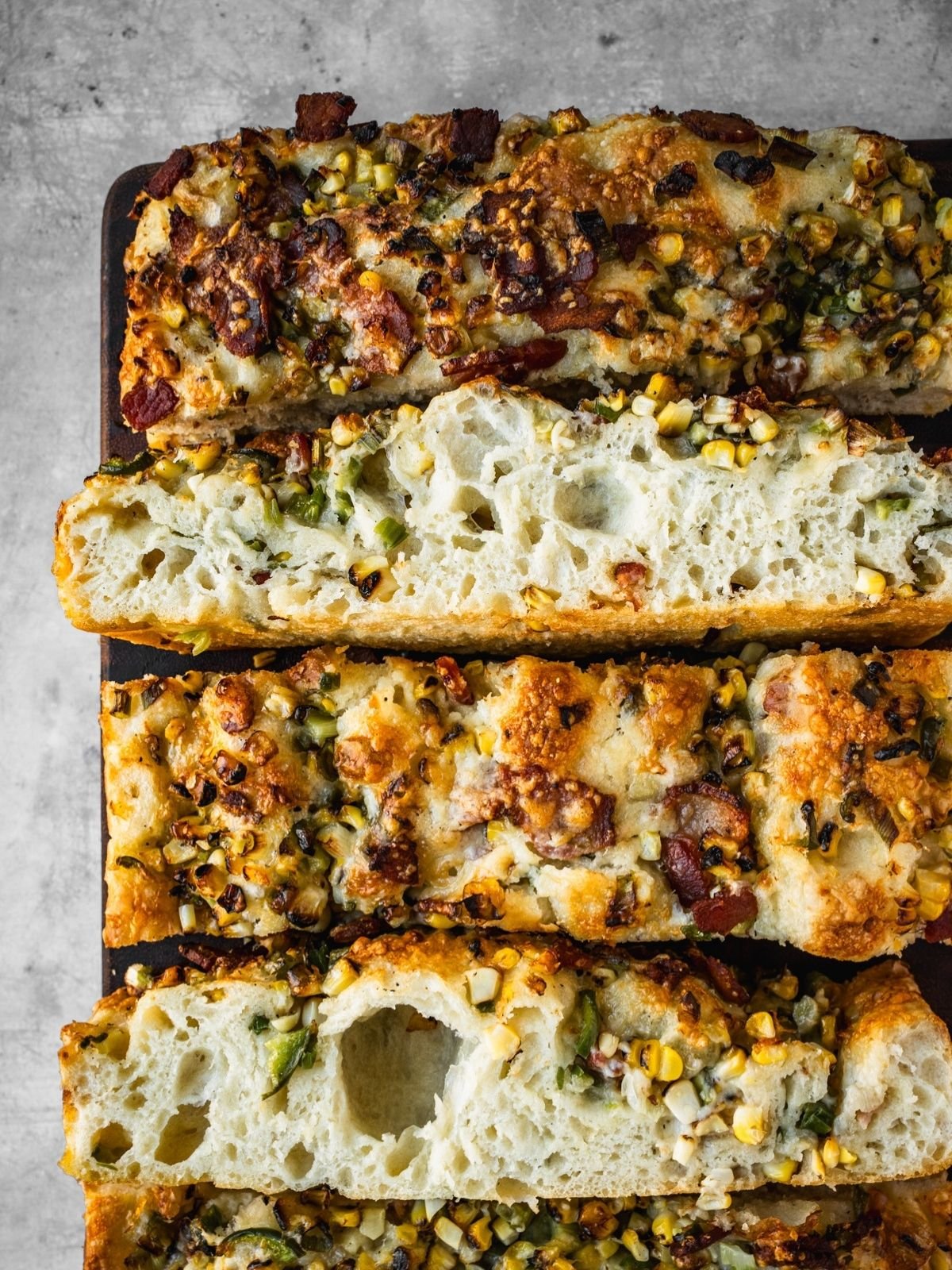 Corn jalapeno bacon focaccia slices on a wooden board.