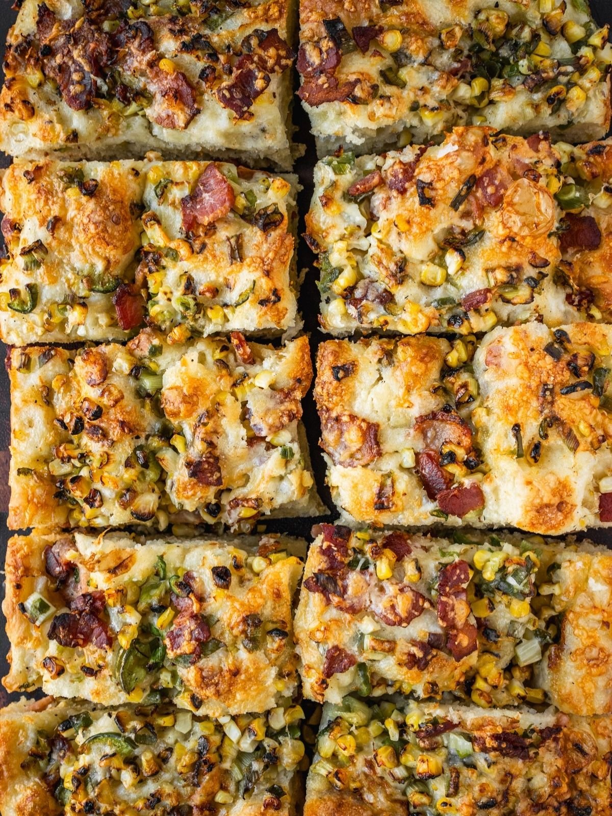 Corn jalapeno bacon focaccia slices on a wooden board.