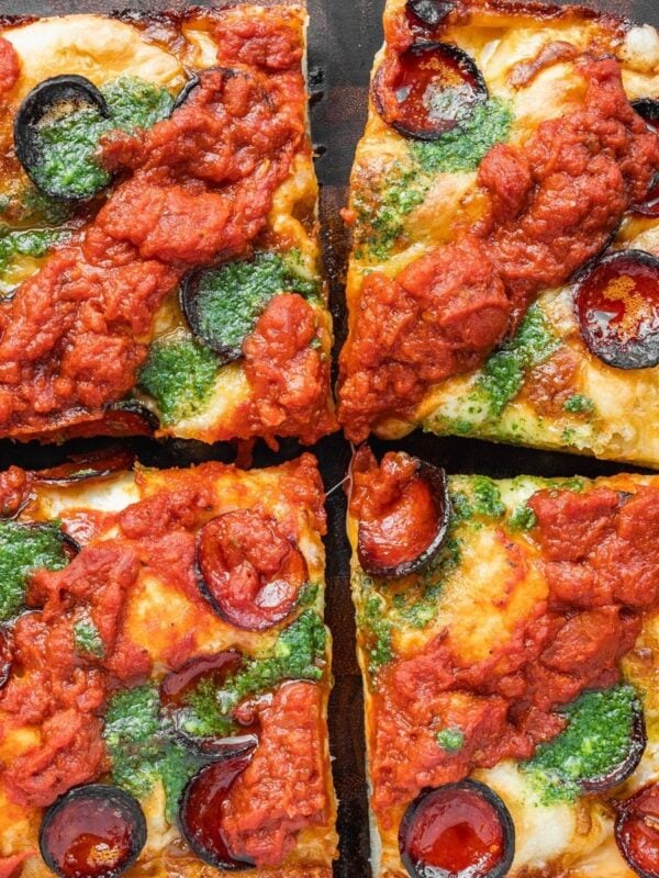 Detroit style pizza with pepperoni, sauce on top and basil garlic oil on a wooden tray.