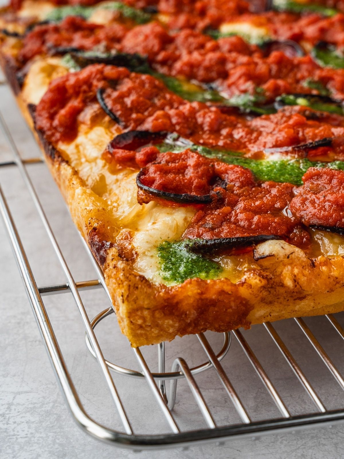 Detroit style pizza with pepperoni, sauce on top and basil garlic oil on a cooling rack.