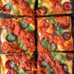 Detroit pizza with pepperoni, sauce on top and basil garlic oil on a wooden tray.