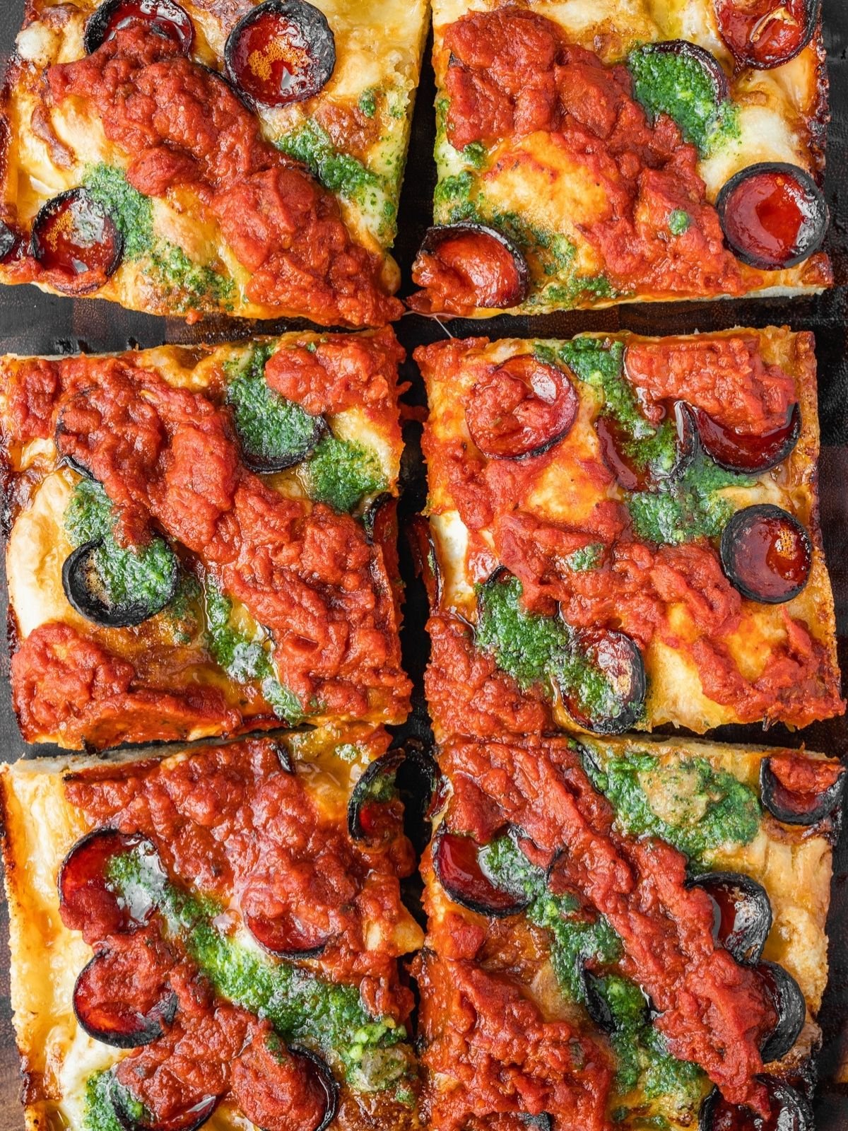 Detroit pizza with pepperoni, sauce on top and basil garlic oil on a wooden tray.