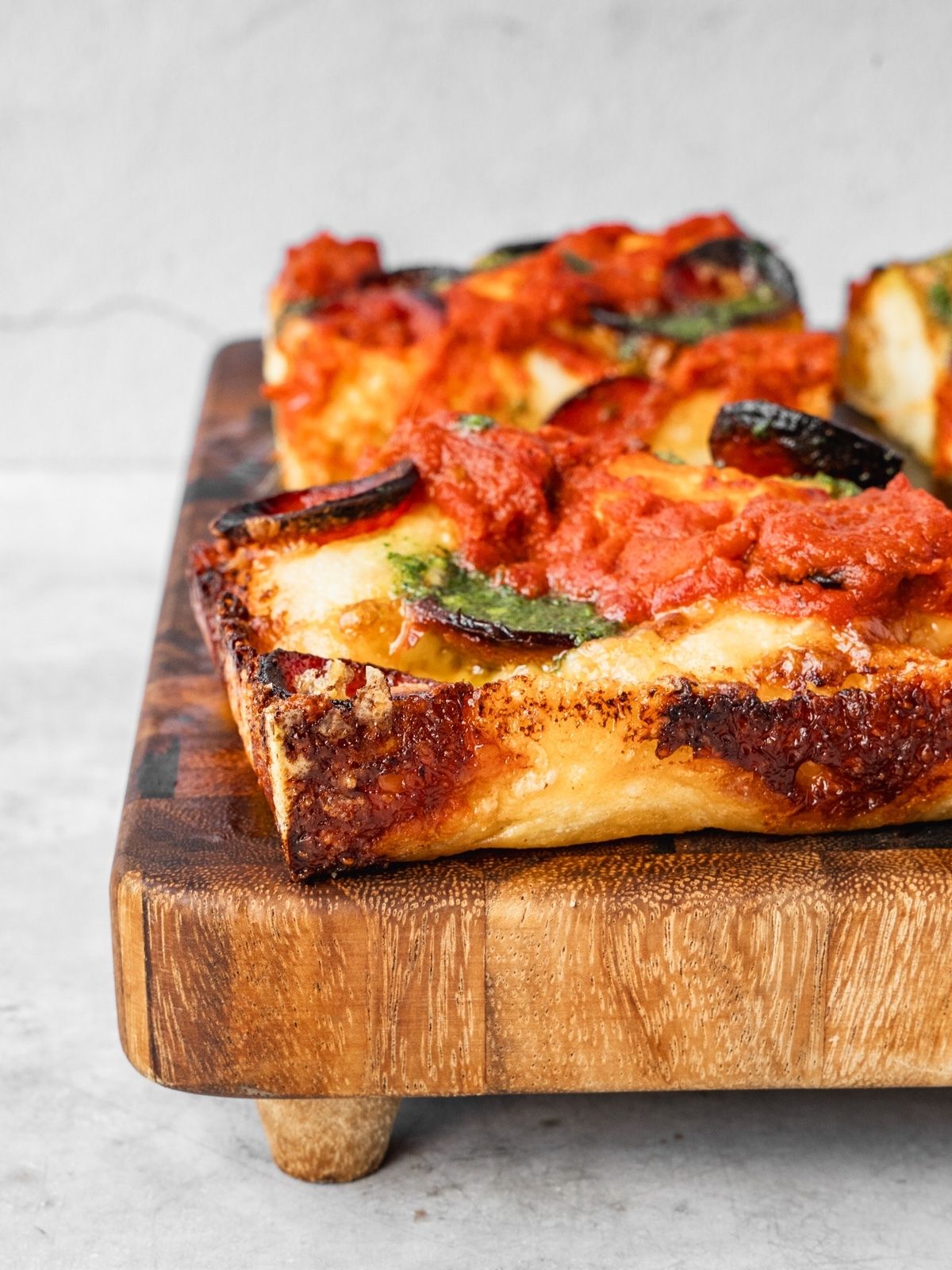Detroit pizza with pepperoni, sauce on top and basil garlic oil on a wooden tray.
