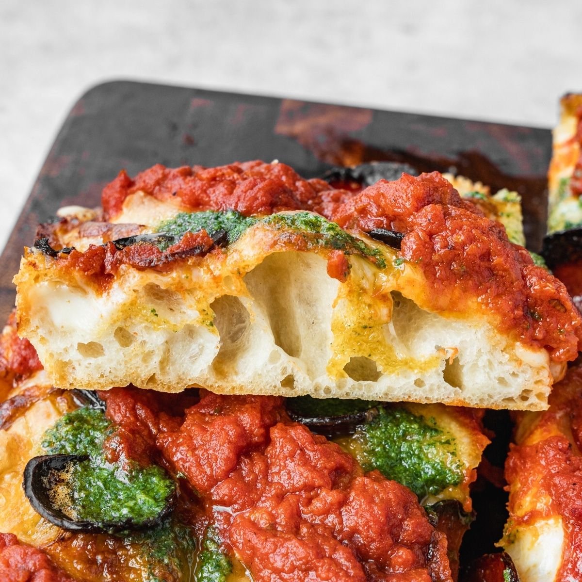 Detroit style pizza with pepperoni, sauce on top and basil garlic oil on a wooden tray.