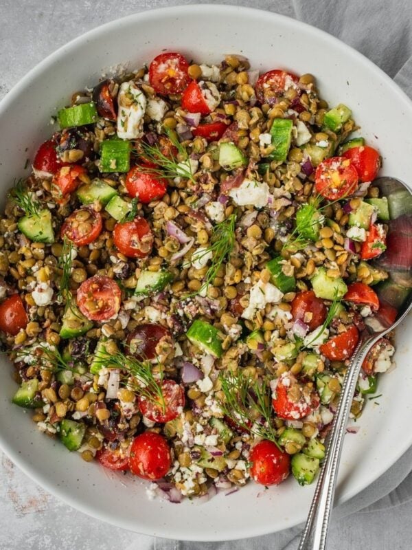 Greek-inspired lentil salad in a large bowl with sliced cherry tomatoes, cucumbers, feta, olives and herbs.