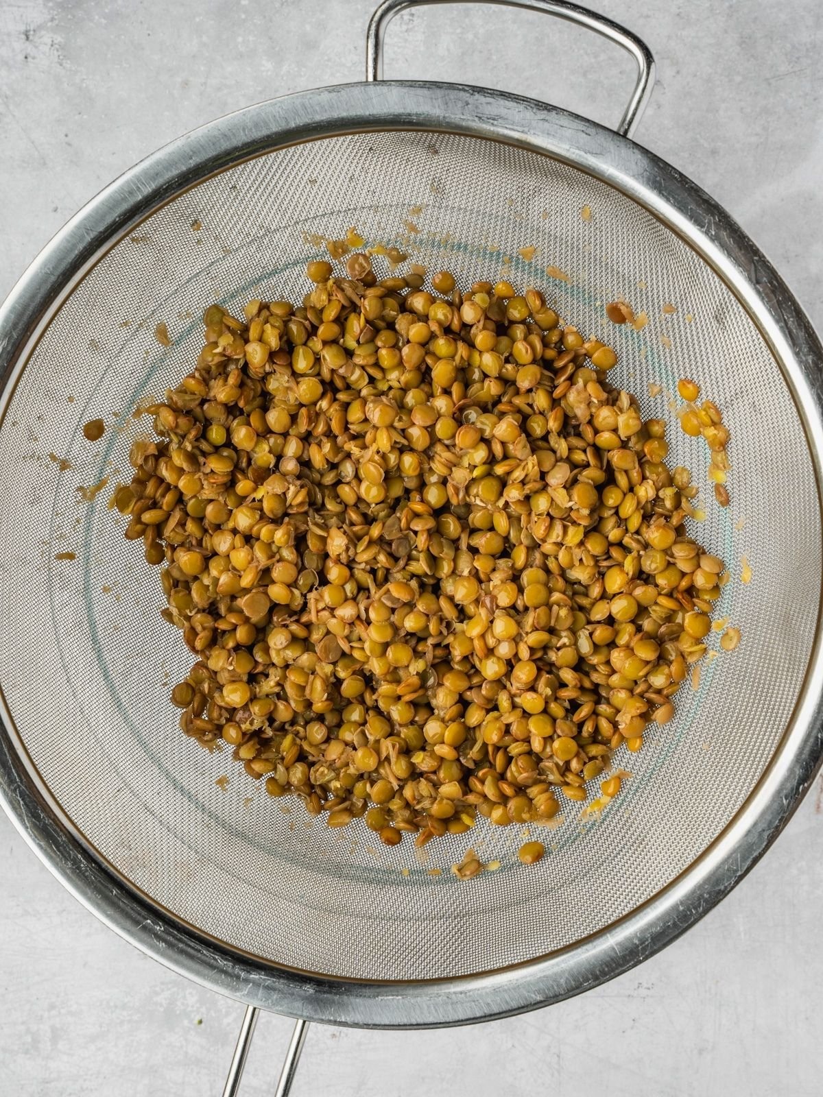 Cooked lentils draining in a metal fine mesh sieve.