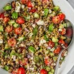 Greek lentil salad in a large bowl with sliced cherry tomatoes, cucumbers, feta, olives and herbs.