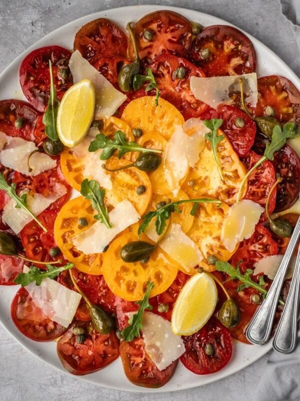 Large platter with sliced heirloom tomato carpaccio with shaved parmesan, arugula, capers and caper berries.