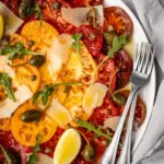 Large platter with sliced heirloom tomato carpaccio with shaved parmesan, arugula, capers and caper berries.