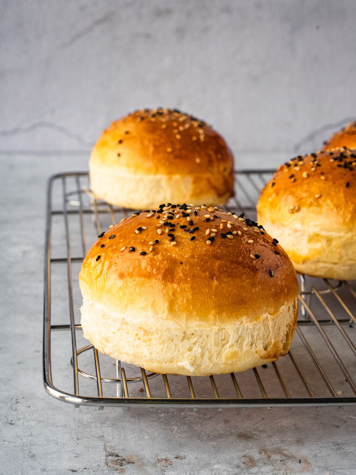 Homemade hamburger buns resting on a cooling rack.