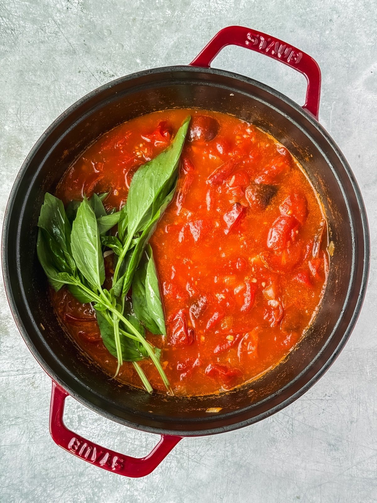 A bunch of basil getting added to tomato sauce.