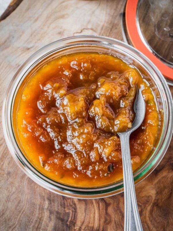 Small batch homemade peach jam in a mason jar on a wooden tray.