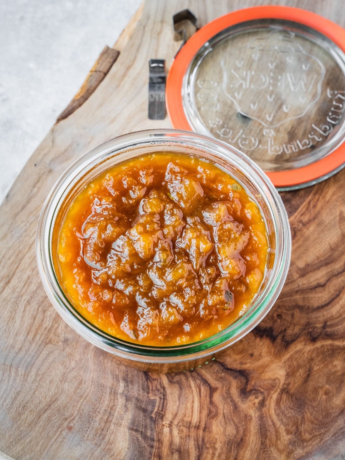 Small batch homemade peach jam in a mason jar on a wooden tray.