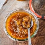 Small batch homemade peach jam in a mason jar on a wooden tray.