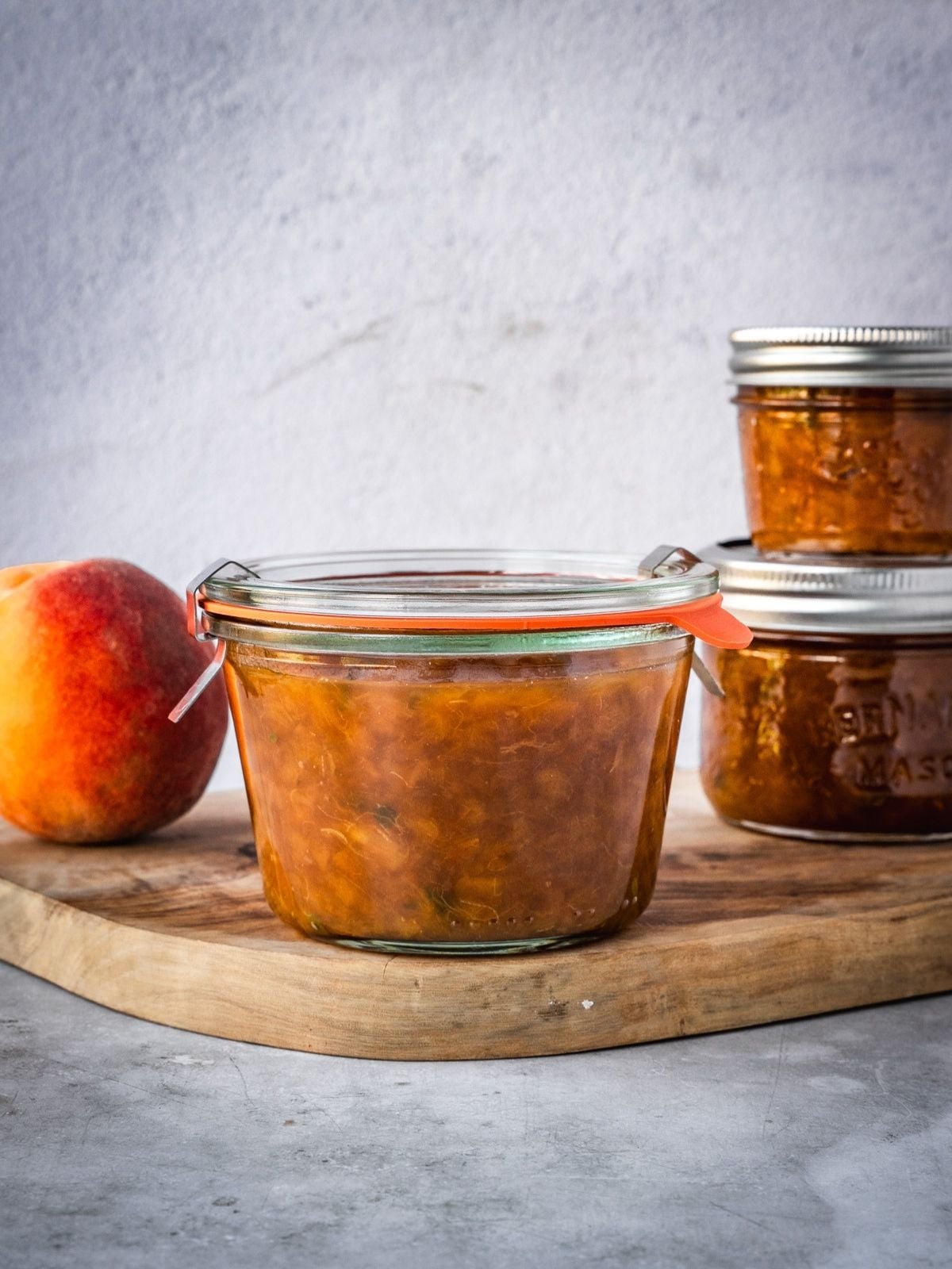 Small batch homemade peach jam in a mason jars on a wooden tray.