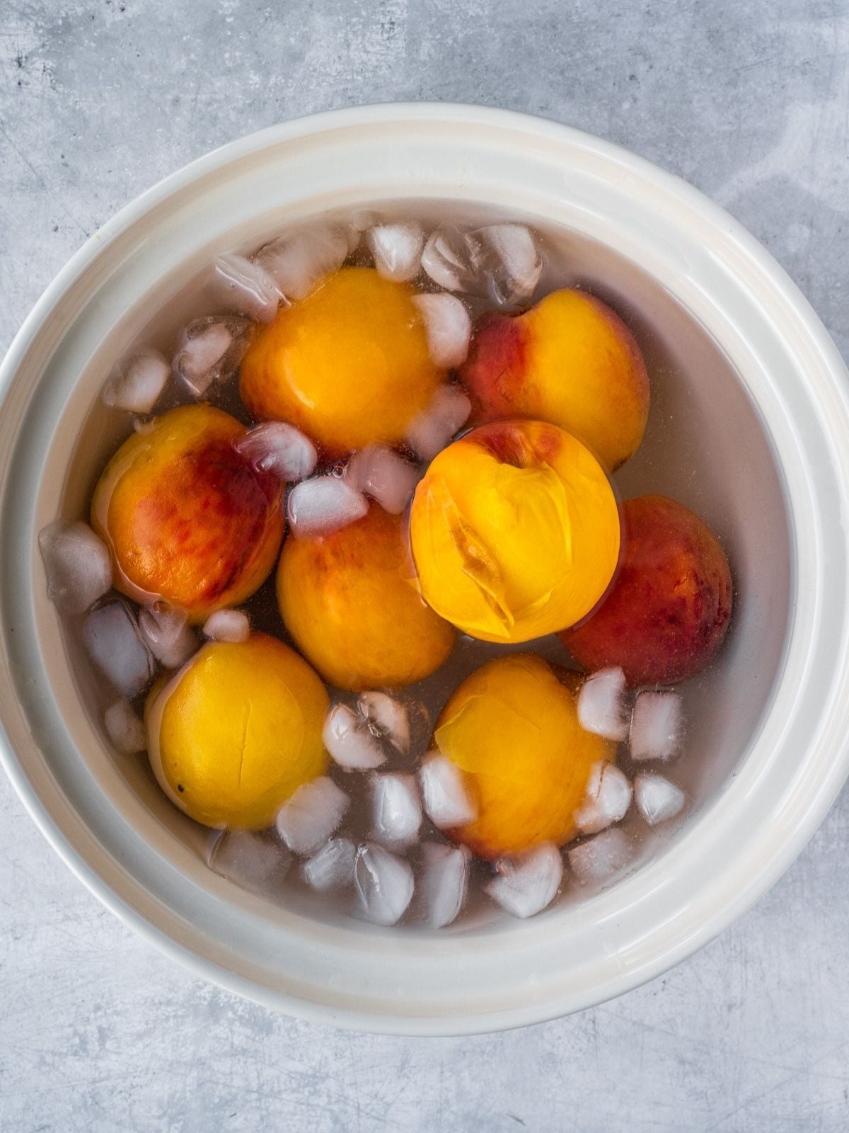 Peaches in a large bowl with ice water.
