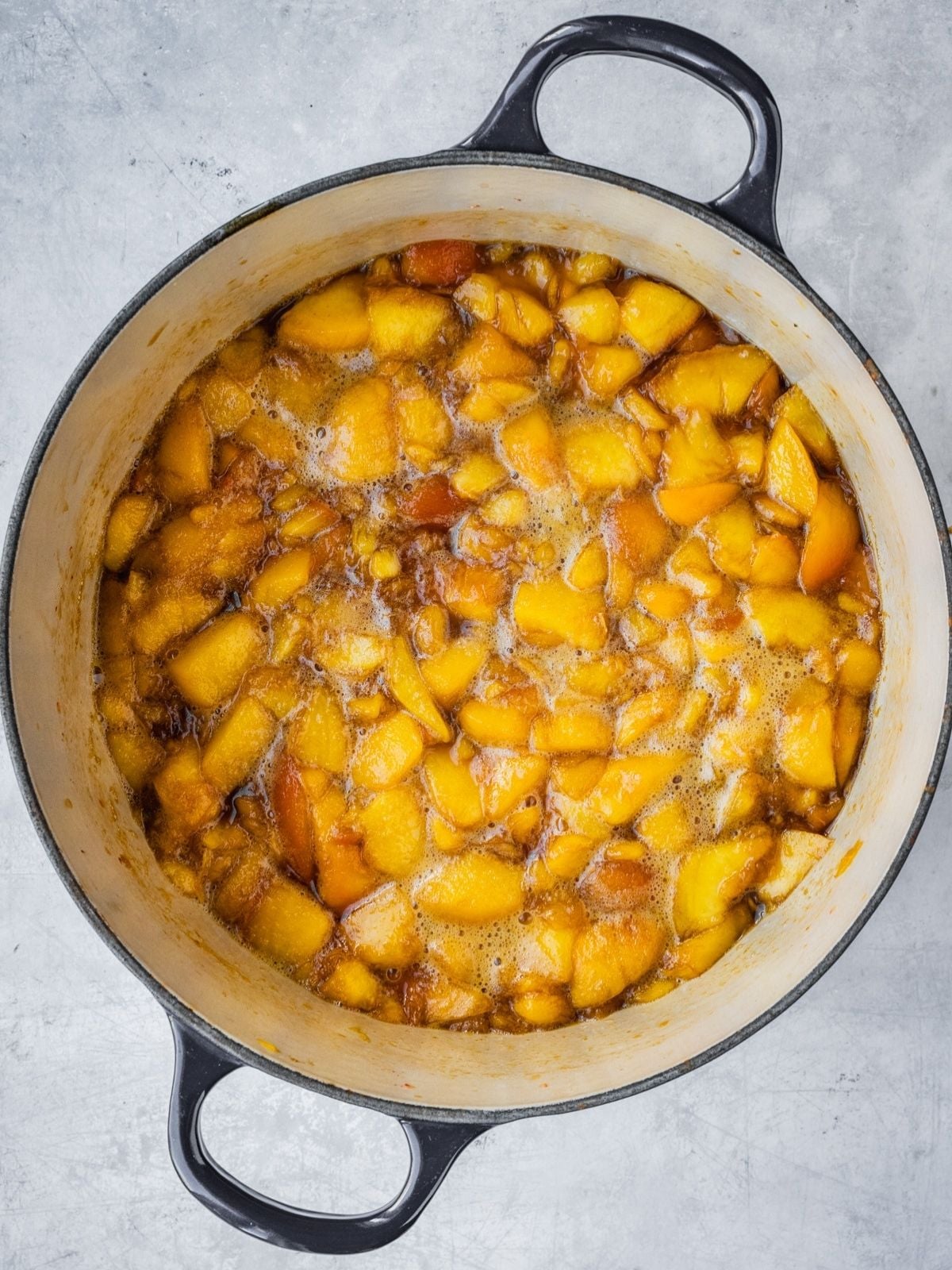 Half-way cooked jam in a pot, showing that the peach pieces are still whole.