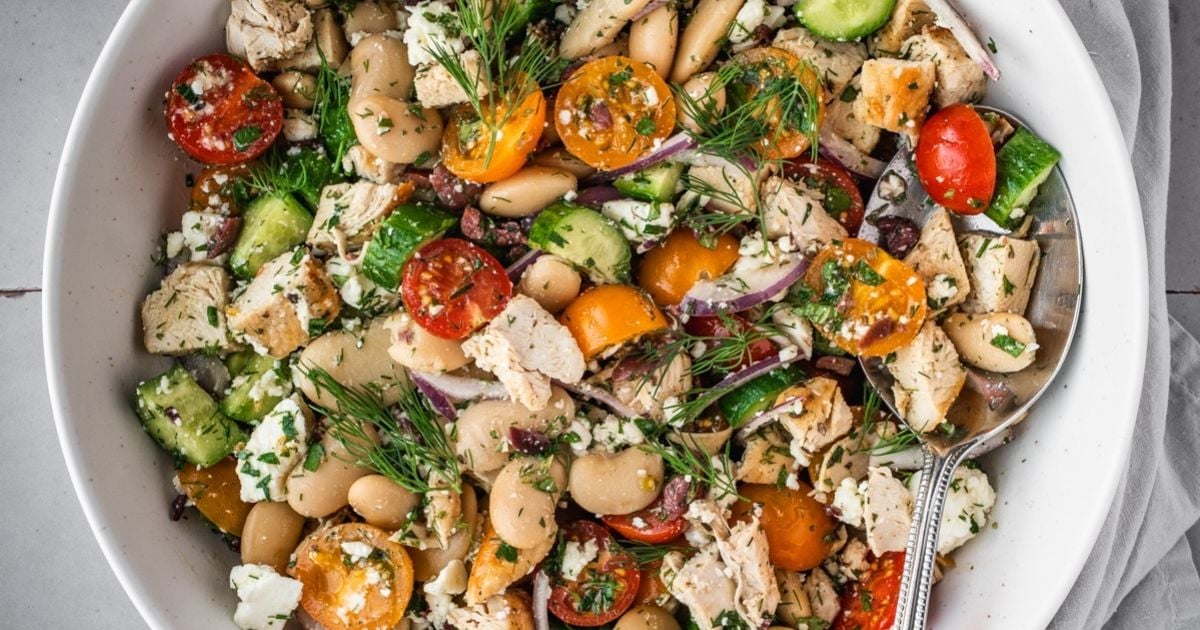 Bowl of bean salad with chicken pieces, cherry tomatoes, cucumbers and herbs. 