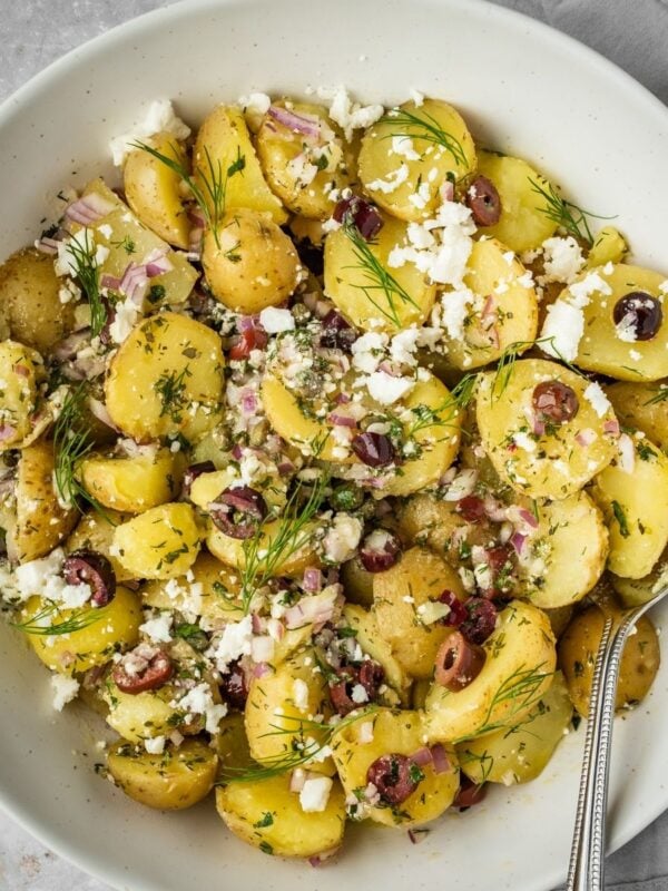 Greek-inspired potato salad with feta, olives, onions and fresh herbs in a serving bowl.