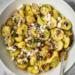 Greek-inspired potato salad with feta, olives, capers, onions and fresh herbs in a serving bowl.