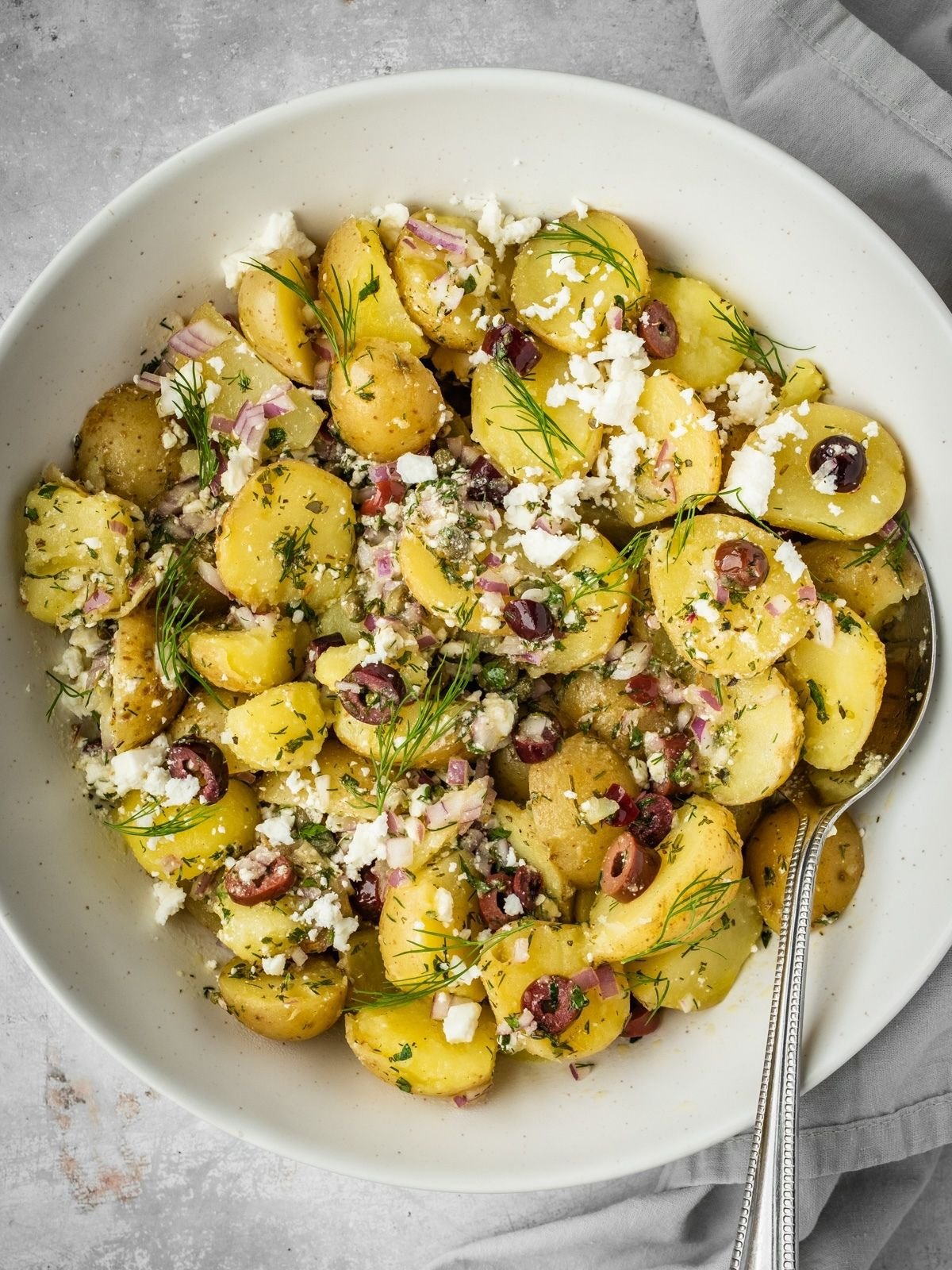 Greek-inspired potato salad with feta, olives, capers, onions and fresh herbs in a serving bowl.