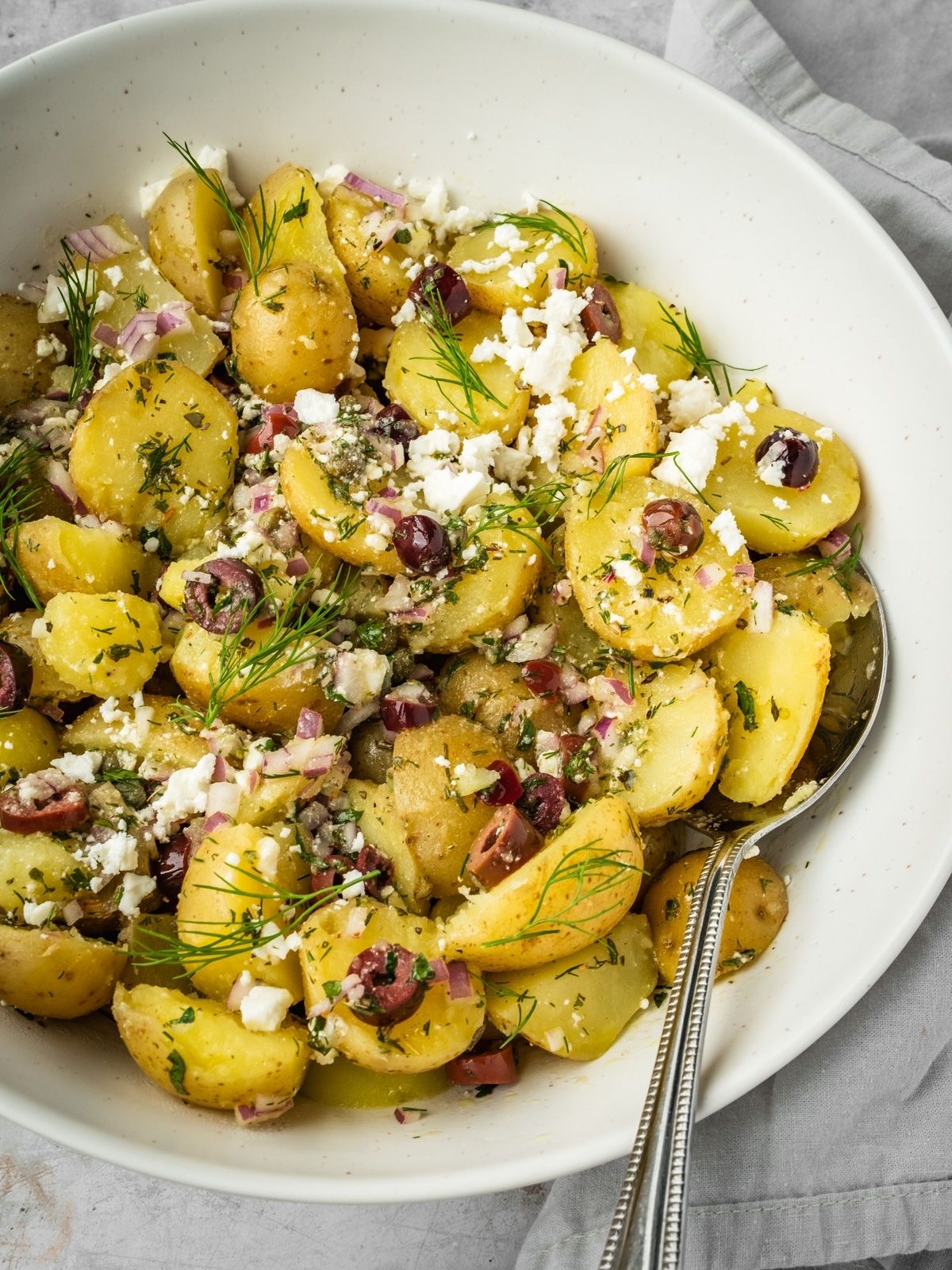 Greek style potato salad with feta, olives, capers, onions and fresh herbs in a serving bowl.
