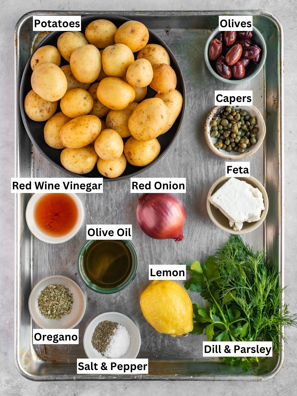 Greek-inspired potato salad recipe ingredients with individual labels on a metal tray.