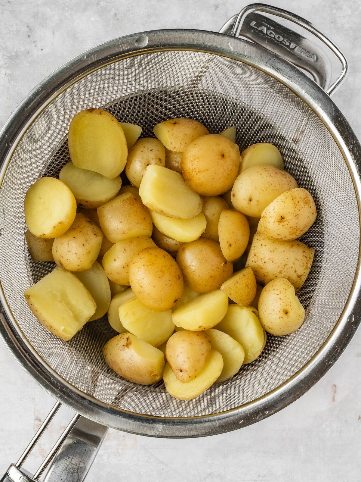 Cooked potatoes sitting in a metal sieve.