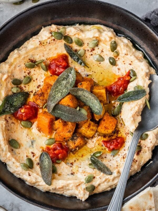 A bowl with mafghoussa sip garnished with roasted squash, pumpkin seeds, fried sage, sumac and chili paste.