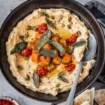 A bowl with mafghoussa sip garnished with roasted squash, pumpkin seeds, fried sage, sumac and chili paste.