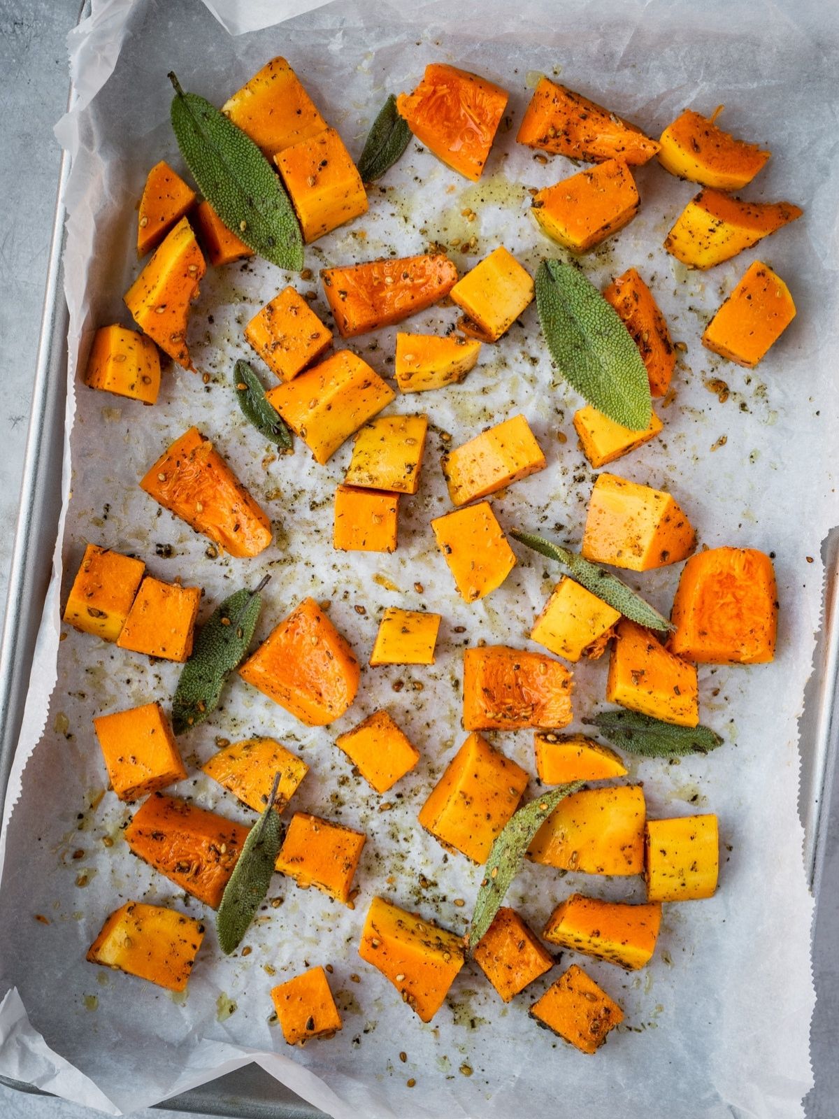 Butternut squash cubes, sage, za'atar and olive oil on a parchment paper lined baking sheet.