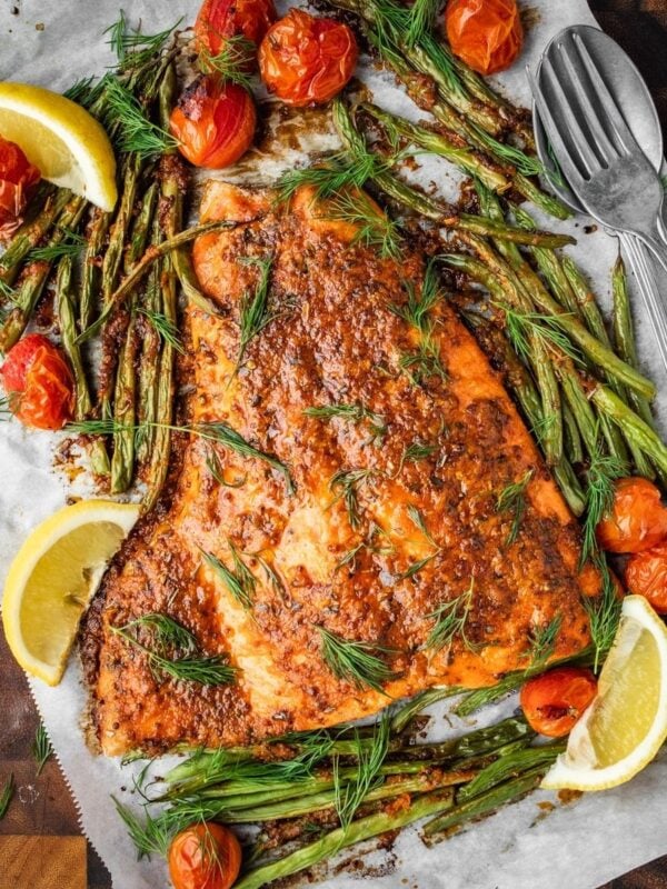 Baked Mediterranean Salmon fillet garnished with fresh dill and served with blistered cherry tomatoes and green beans on a wooden tray.