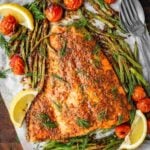 Baked Mediterranean Salmon fillet garnished with fresh dill and served with blistered cherry tomatoes and green beans on a wooden tray.