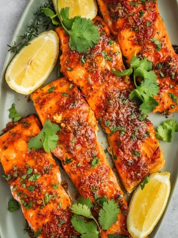 Honey Harissa Salmon fillets on a platter garnished with chopped cilantro and lemon wedges.
