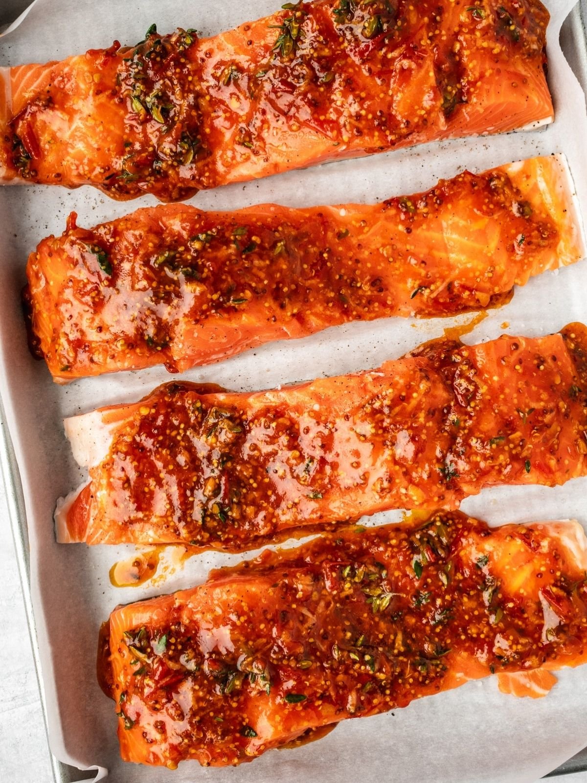 Glazed salmon filets on a parchment paper lined baking sheet ready for the oven.