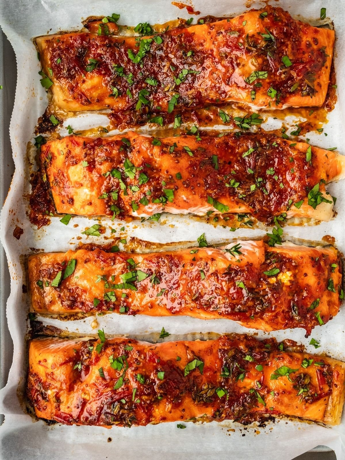 Baked salmon filets on a baking tray garnished with chopped cilantro.