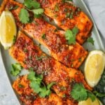 Honey Harissa Salmon fillets on a platter garnished with chopped cilantro and lemon wedges.
