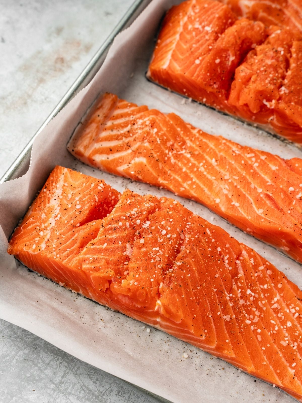 Salmon fillets seasoned with salt and pepper on a parchment paper lined baking sheet.